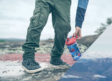 Child splashing in a puddle and holding a kids water bottle.